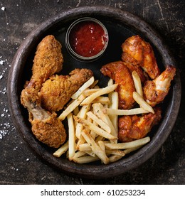 Fast Food Fried Crispy And Spicy Chicken Legs, Wings And French Fries Potatoes With Salt And Ketchup Sauce Served In Stone Plate Over Dark Texture Background. Top View. Square Image