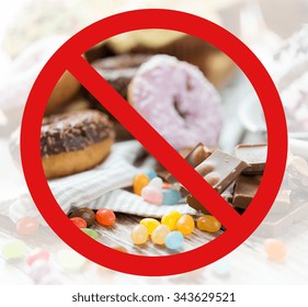 Fast Food, Low Carb Diet, Fattening And Unhealthy Eating Concept - Close Up Of Chocolate Pieces, Jelly Beans And Glazed Donuts Behind No Symbol Or Circle-backslash Prohibition Sign