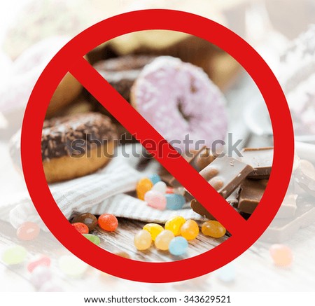 fast food, low carb diet, fattening and unhealthy eating concept - close up of chocolate pieces, jelly beans and glazed donuts behind no symbol or circle-backslash prohibition sign