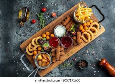 fast food meals mozzarella sticks, onion rings, french fries, chicken nuggets and sauce. pub appetizers on a wooden board. banner, menu, recipe place for text, top view.