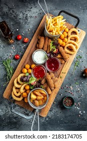 fast food meals mozzarella sticks, onion rings, french fries, chicken nuggets and sauce. pub appetizers on a wooden board. banner, menu - Shutterstock ID 2183174705