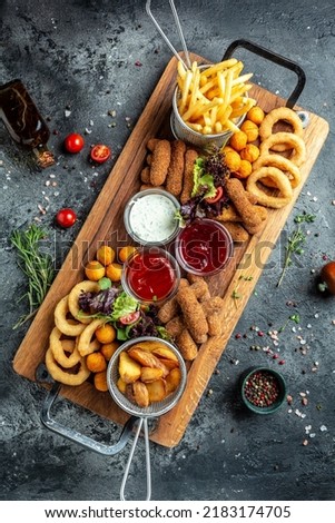 fast food meals mozzarella sticks, onion rings, french fries, chicken nuggets and sauce. pub appetizers on a wooden board. banner, menu