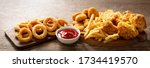 fast food meals : onion rings, french fries, chicken nuggets and fried chicken on wooden table