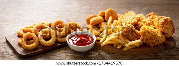 fast food meals : onion rings,\
french fries, chicken nuggets and fried chicken on wooden\
table
