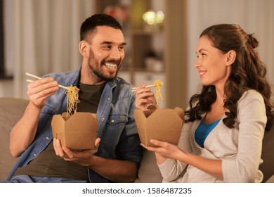 Fast Food And People Concept - Happy Couple Eating Takeaway Noodles With Chopstick At Home In Evening