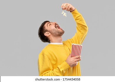 Fast Food People Concept - Young Man In Yellow Sweatshirt Eating Popcorn Throwing It To Open Mouth Over Grey Background