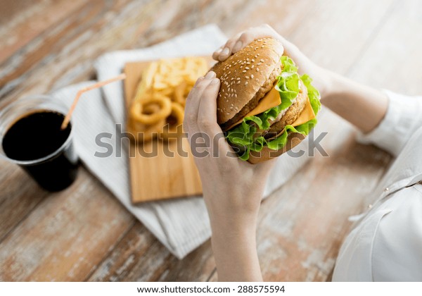 fast food, people and\
unhealthy eating concept - close up of woman hands holding\
hamburger or cheeseburger