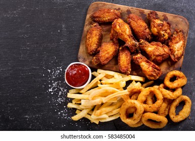 fast food products : onion rings, french fries and fried chicken on dark table, top view - Shutterstock ID 583485004