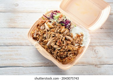 Fast food in a take away box from styrofoam, doner kebab with chicken meat, salad and dip on a wooden table, copy space, high angle view from above, selected focus