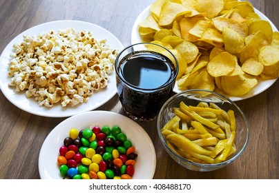 Fast food and unhealthy eating concept -  french fries and potato chips and candies  and popcorn and sweet lemonade on wooden table top view.Unhealthy Lifestyle - Shutterstock ID 408488170