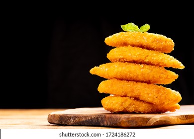 Fast homemade food.Fast food.Chicken breaded nuggets with basil leaves on a wooden kitchen board on a wooden table on a black background.