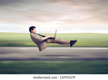 Fast levitating businessman, on a road, using a laptop computer
