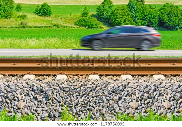 A fast moving car along the road\
goes alongside the railway tracks. Tracks running next to the road.\
A sunny view of a car passing through the\
countryside