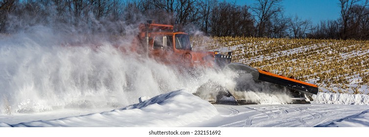 A Fast Moving Orange Snow Plow On A Rural Road Creates A Temporary Blizzard.