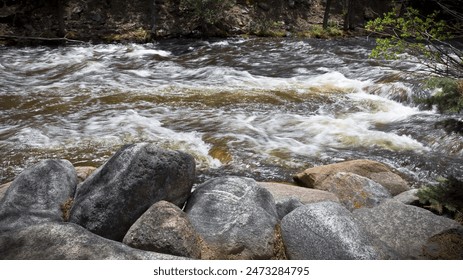 Fast moving soft de-focused water in a cold mountain stream rushes past large boulders on the shore line - Powered by Shutterstock