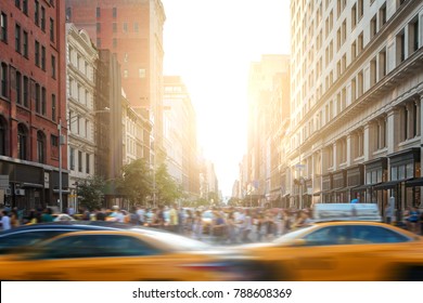 Fast Paced Motion In New York City As Yellow Taxi Cabs Speed Down 5th Avenue With Crowds Of Busy People Walking Across The Intersection At 23rd Street In Manhattan With Sunset Light In The Background