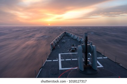 A fast ship frigate navigating. A high speed boat navigating in the sea during sunset. A moving sea during sunset. Navigate into the sun.