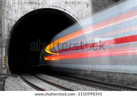 Fast train entering a tunnel with old concrete portal near Altena Germany in rural Lenne valley. Long time exposure shows motion of white and red passenger train in a curve vanishing in the darkness.