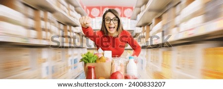 Fast woman with superpowers doing grocery shopping, she is pushing the shopping cart and raising her fist