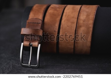 Fastened fashionable men's brown leather belt with a metal buckle on black background. 