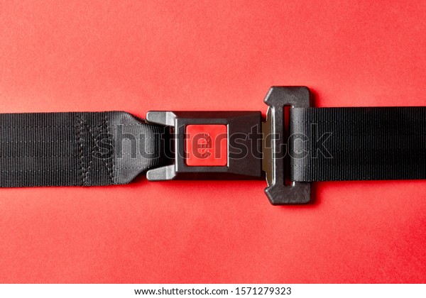 Fastened seat belt on red background with copy\
space. Car safety belt with red press button for fasten lock,\
close-up. Health insurance\
concept