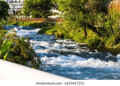 Fast-flowing section of Düden River in Antalya, Turkey, surrounded by lush greenery and sunlight filtering through trees.