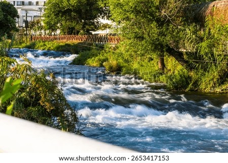 Fast-flowing section of Düden River in Antalya, Turkey, surrounded by lush greenery and sunlight filtering through trees.