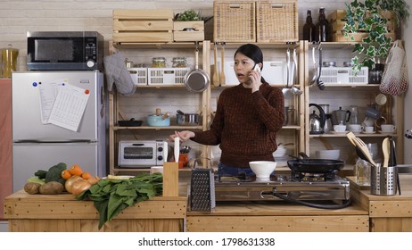 Fast-paced Lifestyle Asian Woman Having Business Phone Call While Checking On Oven, Cooking Meal And Having Morning Coffee.