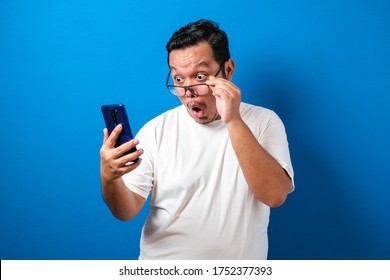 Fat Asian guy wearing a white t-shirt looks surprised at the good news he received from his smartphone. Men show shocked movements with bulging eyes while rolling down his glasses on a smartphone - Shutterstock ID 1752377393