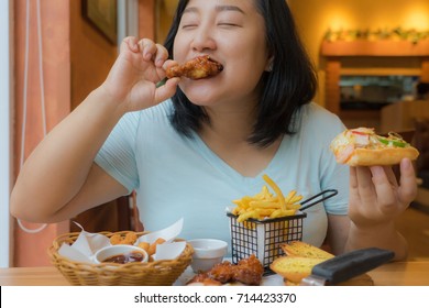 Fat Asian Woman Enjoy Eating Delicious Chicken Wing,overweight Female Is Holding Pizza In Hand,fast Food Restaurant