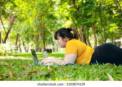 Fat Asian woman lying on the grass in the park Watch online media on laptop computer. Weight loss concept. Exercise for good health of obese people.