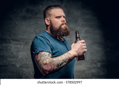 Fat bearded men with tattoos on arm holds beer bottle.