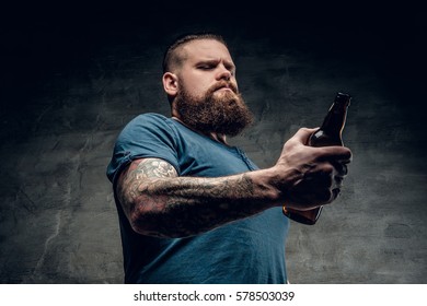 Fat bearded men with tattoos on arm holds beer bottle.