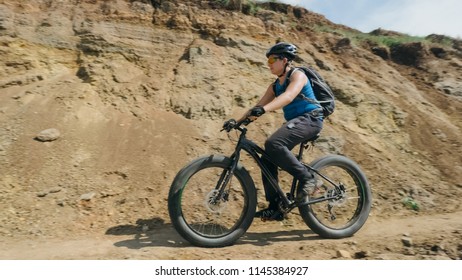 Fat Bike Also Called Fatbike Or Fat-tire Bike In Summer Driving On The Road. The Guy Rides By The Hill On A Sand Clay Path, Behind Him The Shore By The Sea.