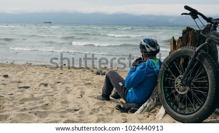 Fat bike also called fatbike or fat-tire bike in summer driving on the beach. The guy sits on the wheel of his bicycle, looks at the sea. Stock photo © 