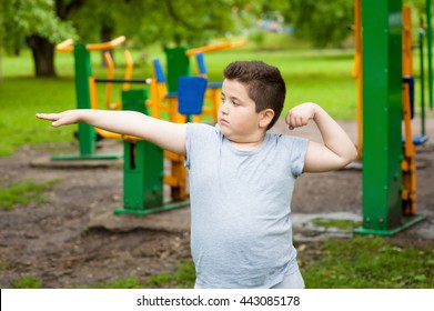 Fat Boy Shows His Muscles In The Background Of  Exercise Equipment