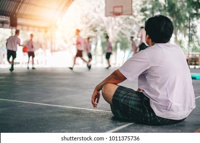 Fat Boy Student Watching His Friends Play Basketball At The Gymnasium In School.