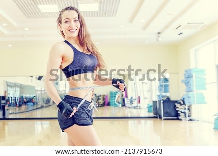 Fat burning, intense exercise. A woman measures the size of the muscles with a measuring tape. Sports girl in the gym. The growth of muscle mass.