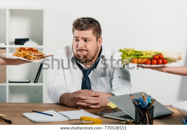 fat businessman choosing healthy or junk food at workplace in office