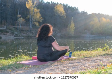 Fat Caucasian Woman With Long Curly Dark Hair Dressed In Black Tshirt And Black Sportive Pants Online Is Doing Yoga On Purple Mat The Autumn Park. The Phone Shows An Online Yoga Class