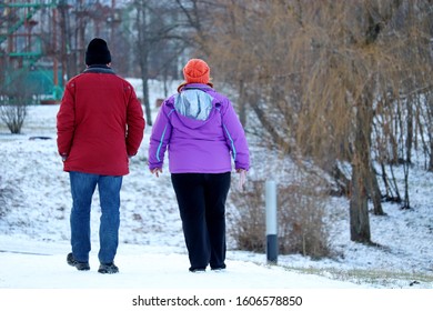 Fat Couple Walking Down In Winter Park. Man And Overweight Woman On A Street, Concept Of Healthy Lifestyle