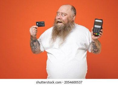 Fat fun pudge chubby overweight tattooed bearded big belly man in white t-shirt hold wireless bank payment terminal process, acquire credit card payments isolated on orange background studio portrait.
