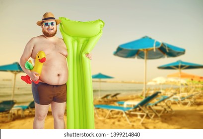 Fat funny man in swimming trunks with an inflatable mattress on a gray background.