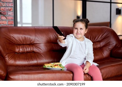 Fat Kid Girl Is Going To Eat Hamburger And Watch Tv, Sitting On Sofa In Living Room After School, Have Rest. Overweight Girl In Domestic Wear Having Leisure Time, No Control Over Eating Behavior