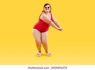 Fat lady in swimwear enjoying summer holiday and having fun at beach party. Full length portrait happy cheerful joyful young plus size woman wearing red swimsuit dancing isolated on yellow background - Powered by Shutterstock