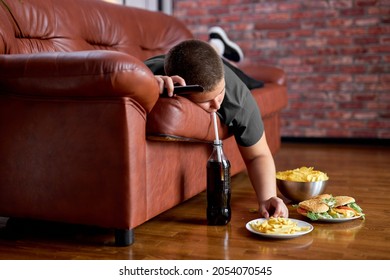 Fat Lazy Boy Taking Fries From Plate Lying On Sofa, Alone At Home, Teenager Boy Having Rest After School, Relaxed. Caucasian child lead unhealthy lifestyle, eating junk meal. overweight, obesity
