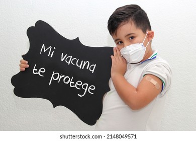 Fat Little Hispanic Boy With Face Mask And School Uniform Shirt Shows His Recently Vaccinated Arm Against Covid-19 With A Black Sign That Says 