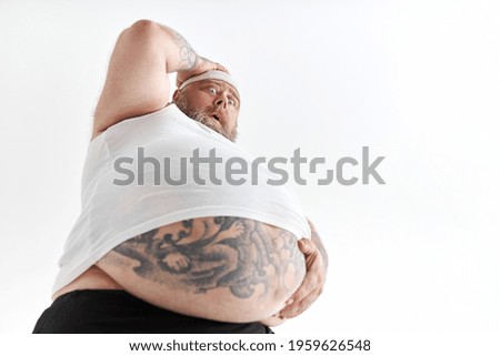 fat man with big belly and tattoes in sports wear is holding his stomach with shocked emotion