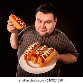 Fat Man Eating Fast Food Hot Dog On Plate. Breakfast For Overweight Person. Junk Meal Leads To Obesity. Person Regularly Overeats Concept On Black Background. Mass Obesity Due To Poor Foods.