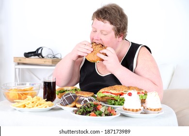 Fat Man Eating A Lot Of Unhealthy Food, On Home Interior Background  